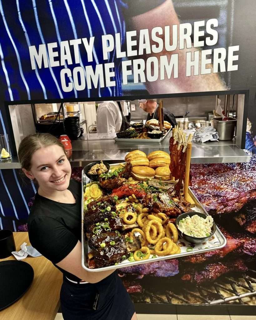 Staff member holding a platter of ribs, onion rings and a burger at Third Wave BBQ Moorabbin