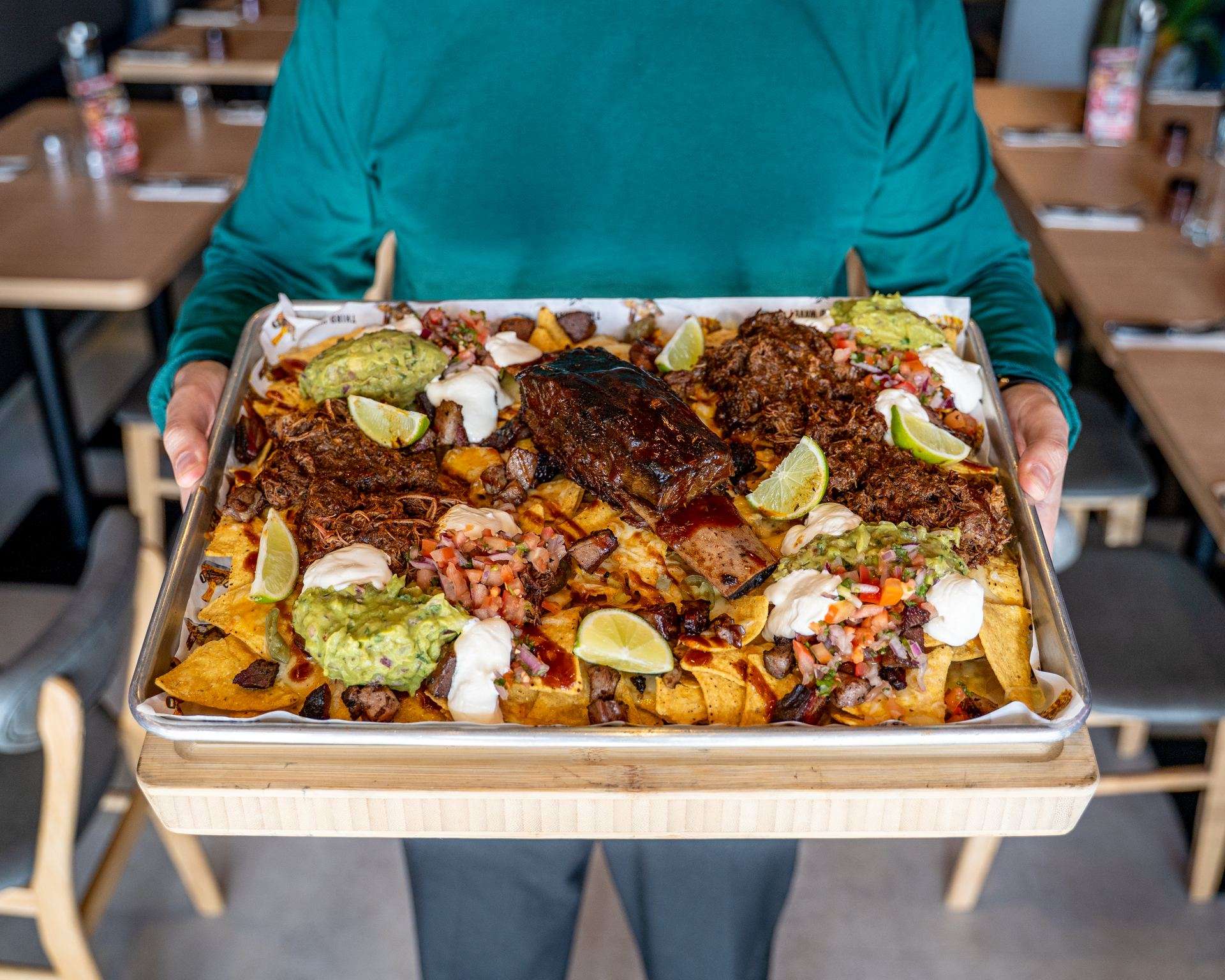 Triple beef nachos on a tray with guacamole and lime, being carried
