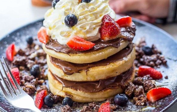 Stack of pancakes with chocolate sauce, cream and mixed berries