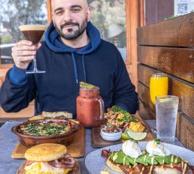 Guest raising a cocktail glass over a bottomless brunch table spread