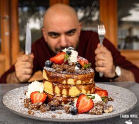 Guest with a knife and fork in front of a stack of pancakes with berries and cream