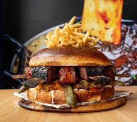 Almighty Burger topped with fries and a rib bone on a wooden board
