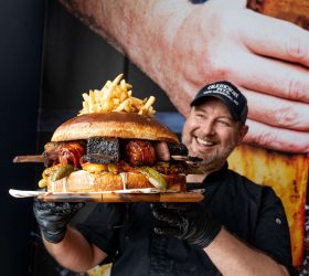 Guest biting into the Almighty Burger topped with fries and a rib bone