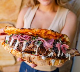 Person holding a 48-hour BBQ pizza pocket with pickled onion