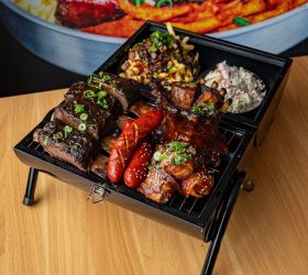 BBQ in a BBQ platter served on a mini grill with ribs, sausages and slaw