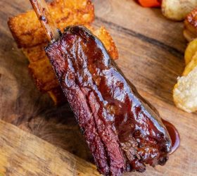 Glazed BBQ beef rib held up with waffle fries in the background