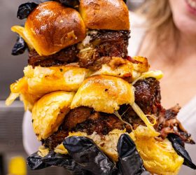 Guest holding skewered Beef Rib Burnt Ends with melted cheese