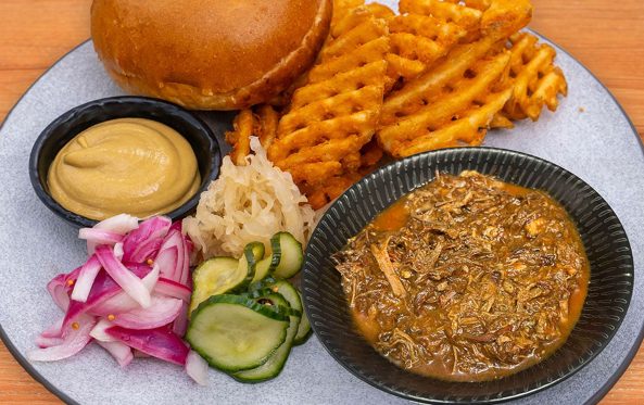 Shredded beef serve with a bun, waffle fries, mustard and pickles