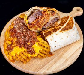 Brisket Lasagna Burrito halves with cheese sauce and waffle fries on a board