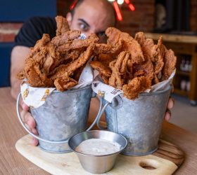 Buckets of chicken fried bacon with a dipping sauce, held up