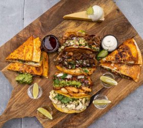 Tacos and quesadilla wedges with dipping sauces and lime on a board