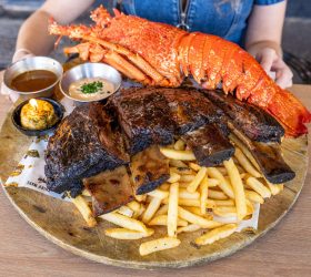 Lobster tail, ribs and fries on a plate, held up