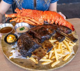 Lobster tail and ribs with fries and dipping sauces, held up