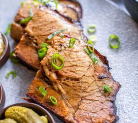Sliced smoked brisket with dark bark and spring onion garnish, pickles aside