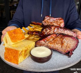 Guest holding a plate of Dino Ribs with cornbread and dipping sauce