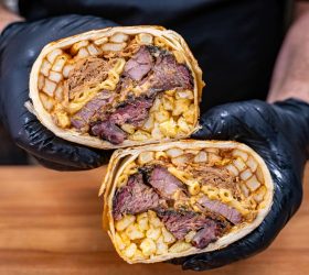 Guest holding two halves of the Everything Burrito with brisket and mac and cheese