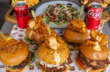 Sliders, mac and cheese, salad and cola arranged on a board