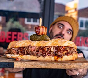 Guest holding the Epic Chopped BBQ Sub topped with a bacon-wrapped skewer