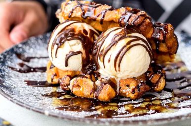 Hand reaching for a dessert of waffle pieces, ice cream scoops and chocolate sauce