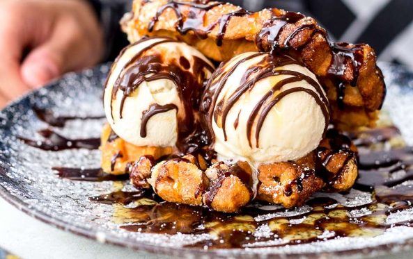 Hand reaching for a dessert of waffle pieces, ice cream scoops and chocolate sauce