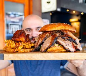 Guest holding a board with the Brisket Overloaded Oh Daddy Burger and fries
