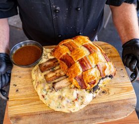 Chef holding the Triple Beef Rib Wellington on a board with gravy