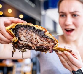 Guest holding a cut Triple Beef Rib Wellington showing three rib bones