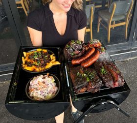 Guest holding a mini BBQ grill loaded with ribs, sausages and loaded fries
