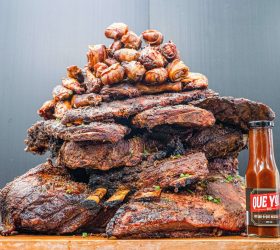 Meat Mountain: a towering stack of smoked ribs and meats beside a hot sauce bottle