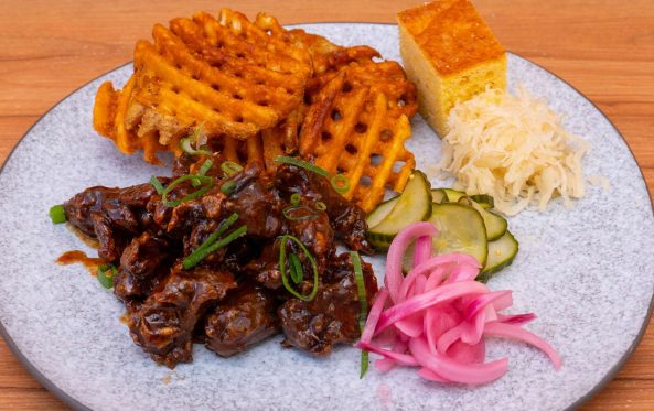 Plate of glazed rib pieces with waffle fries, cornbread and coleslaw