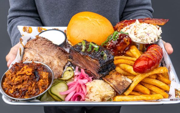 Guest holding the largest BBQ meat platter with ribs, brisket and sides