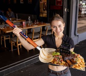 Staff member holding the Grizzly Shovel Nachos on a spade utensil outside Third Wave BBQ
