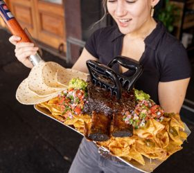 Staff member holding the Grizzly Shovel Nachos tray outside Third Wave BBQ