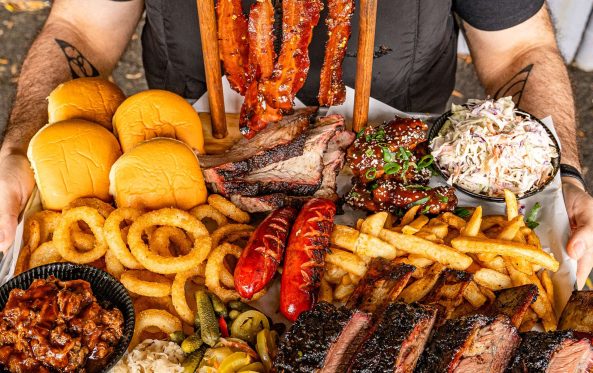 Guest holding a large BBQ platter with ribs, sausages and onion rings
