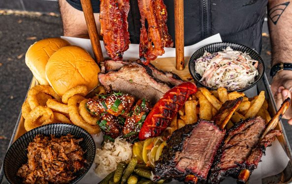 Large BBQ meat platter with ribs, brisket and coleslaw, being carried