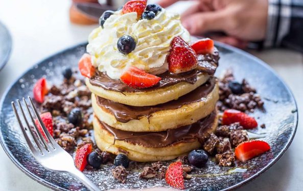 Chocolate pancake stack topped with cream, strawberries and blueberries