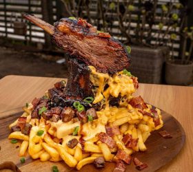 Mac n Cheese Porkano with a porchetta bone standing on cheesy loaded fries