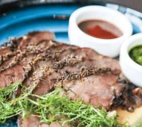 Sliced smoked beef with herbs and two dipping sauces on a board