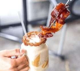 Caramel milkshake topped with a candied bacon skewer, held by a guest