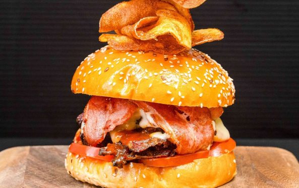 Ribsy burger with bacon, tomato and a chip garnish on a sesame bun