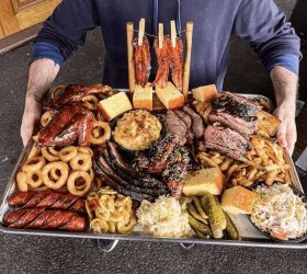 Guest presenting a large BBQ meat platter with ribs, wings and sides for six