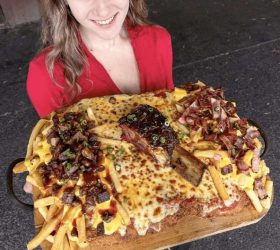 Guest holding two trays of the Big Fluckin Parma loaded cheese fries