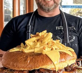 Chef holding the Almighty Burger topped with fries