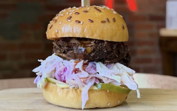 Burger with a thick meat patty and coleslaw on a wooden board
