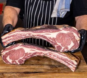Butcher holding two tomahawk steaks on a wooden board