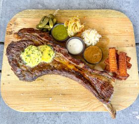 Tomahawk dry-aged steak on a board with butter, slaw and dipping sauces