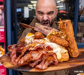 Guest biting into the Chicken and Waffles tower loaded with bacon and brisket