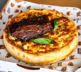 Chicago deep dish pizza topped with basil in a takeaway box