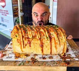 Guest holding the BBQ Brick loaf drizzled with cheese sauce on a board