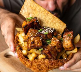 Crispy tortilla bowl filled with glazed meat, fries and sesame seeds, held by a guest